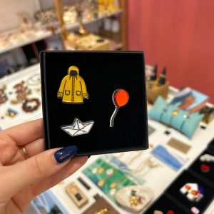 Pin's triple manteau jaune, ballon rouge et bateau en papier ATELIER TROMBONE